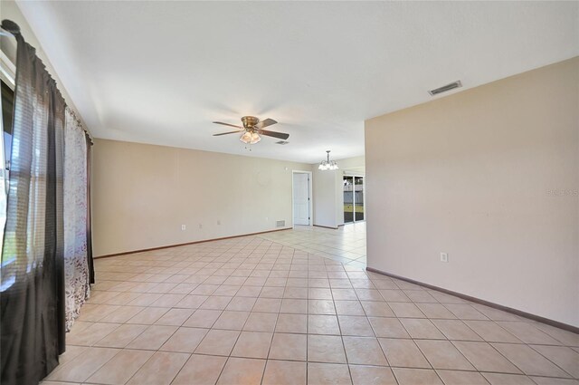 unfurnished room featuring light tile patterned floors, visible vents, baseboards, and ceiling fan with notable chandelier