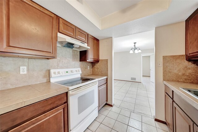 kitchen with under cabinet range hood, brown cabinets, light countertops, and electric stove