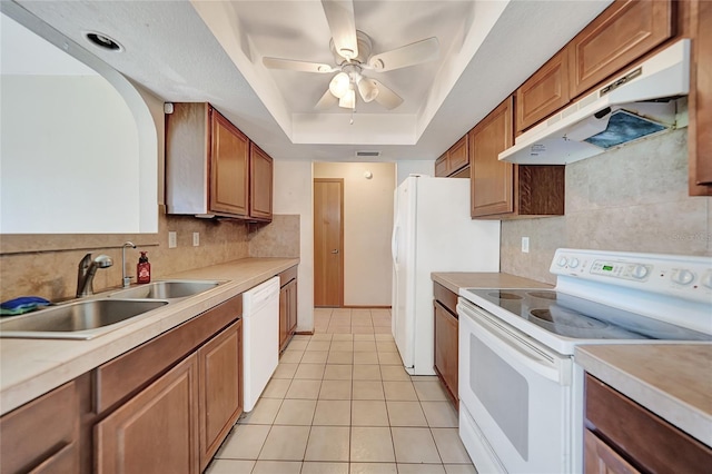 kitchen with white appliances, a tray ceiling, a sink, light countertops, and under cabinet range hood