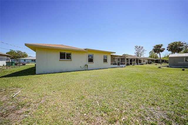 back of property with stucco siding, a lawn, and a sunroom