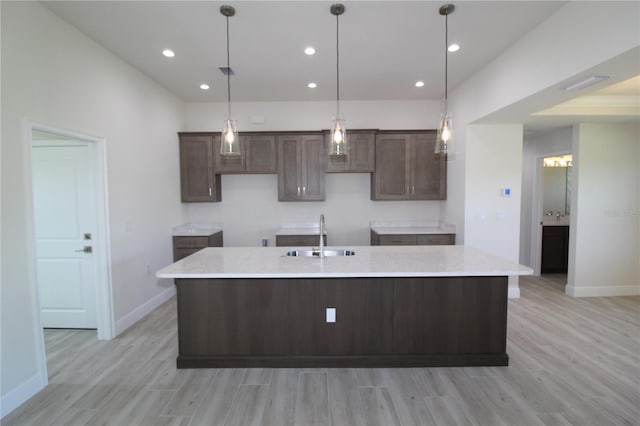 kitchen with a large island, light wood-type flooring, dark brown cabinetry, and a sink