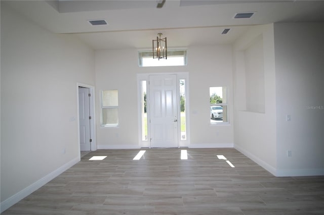 entrance foyer featuring light wood finished floors, visible vents, baseboards, and a towering ceiling