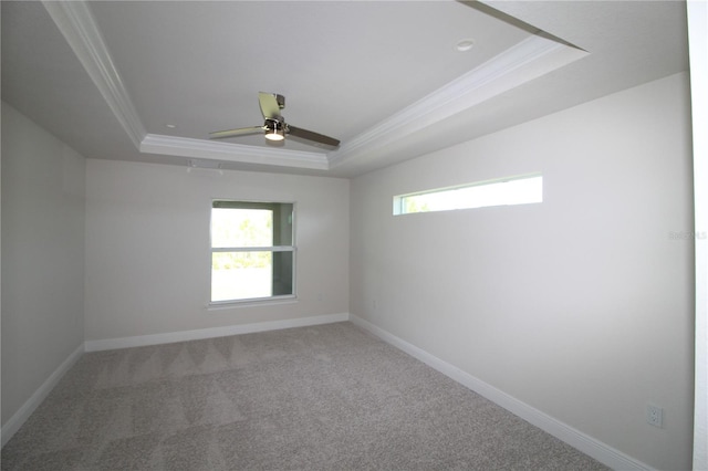 spare room with a tray ceiling, carpet flooring, baseboards, and ornamental molding