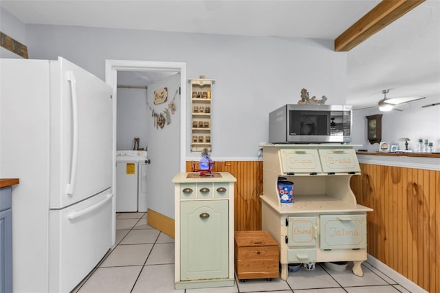 kitchen featuring stainless steel microwave, freestanding refrigerator, wooden walls, wainscoting, and washer / dryer