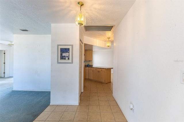 hallway with light tile patterned floors, light colored carpet, visible vents, and a textured ceiling