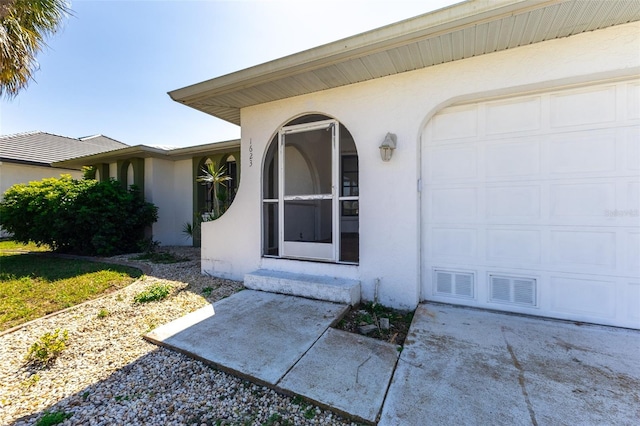 doorway to property with stucco siding, an attached garage, and concrete driveway