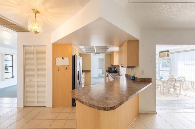 kitchen with dark countertops, a peninsula, an inviting chandelier, light tile patterned flooring, and a sink