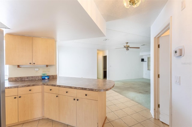 kitchen featuring light tile patterned floors, light brown cabinets, a peninsula, ceiling fan, and light colored carpet