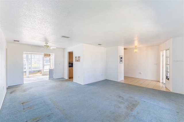 unfurnished living room with light tile patterned floors, visible vents, light colored carpet, and a textured ceiling