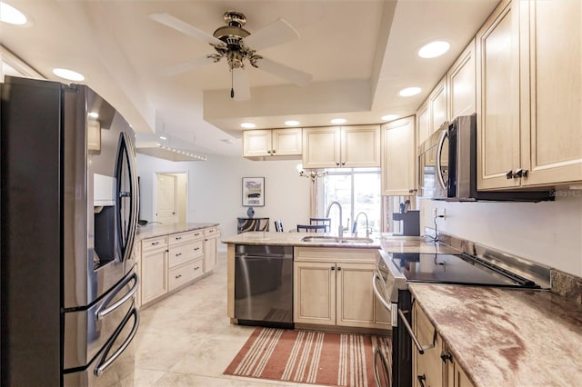 kitchen with ceiling fan, a tray ceiling, a peninsula, stainless steel appliances, and a sink