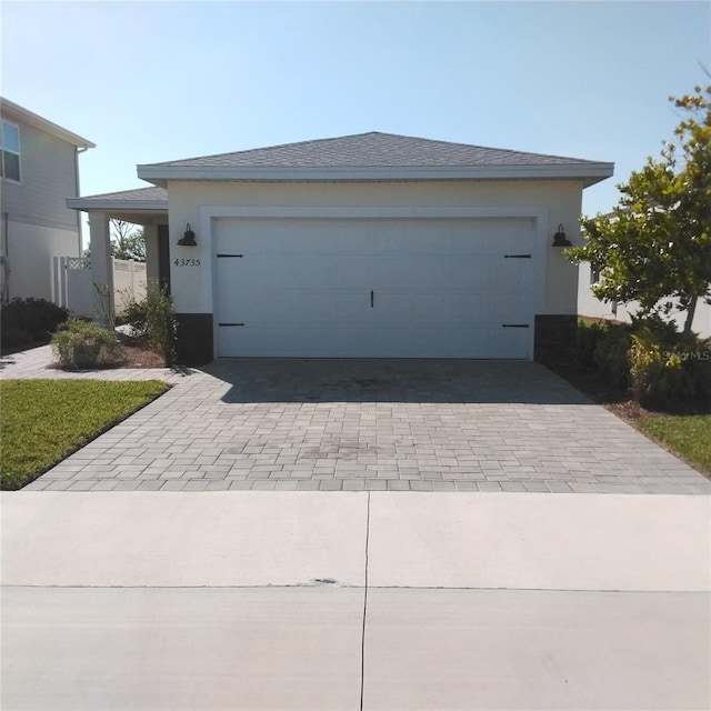 view of front of property with decorative driveway, a garage, roof with shingles, and stucco siding