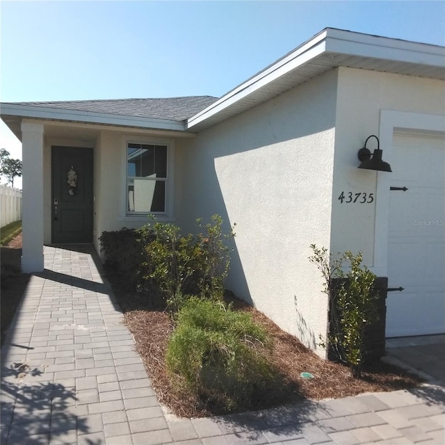 doorway to property featuring a garage, stucco siding, and roof with shingles