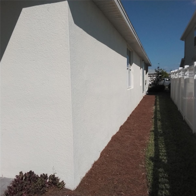 view of side of home featuring stucco siding and fence