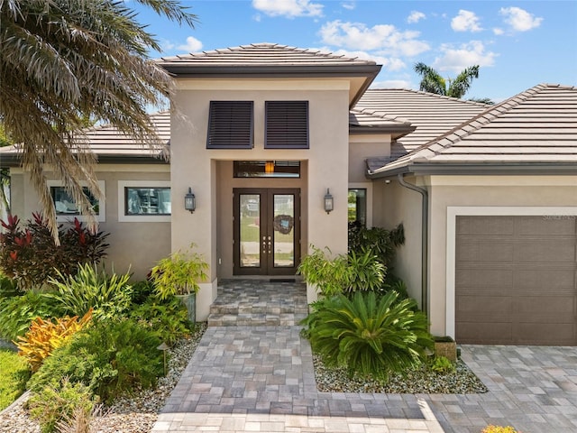 view of exterior entry with a tiled roof, stucco siding, french doors, and an attached garage