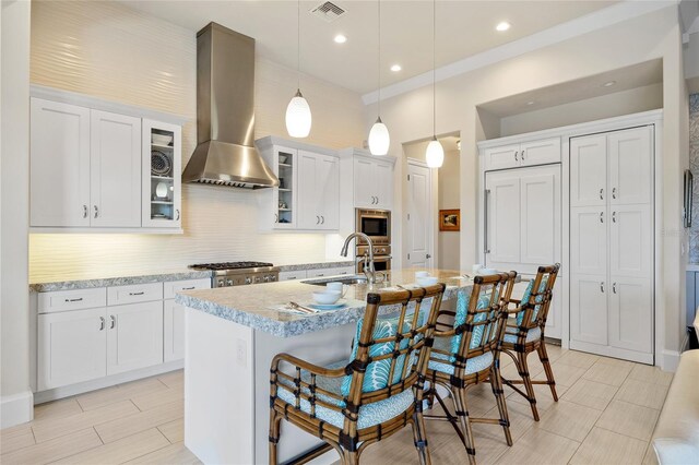 kitchen featuring stainless steel microwave, visible vents, light countertops, wall chimney exhaust hood, and a sink