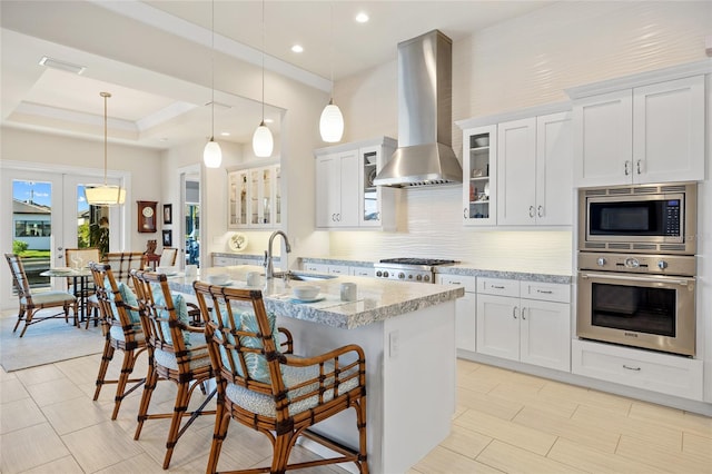 kitchen featuring visible vents, a sink, stainless steel appliances, wall chimney exhaust hood, and backsplash