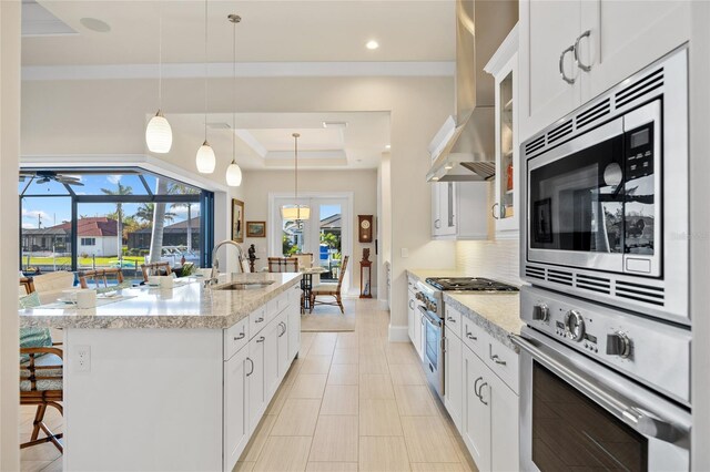 kitchen featuring a breakfast bar, a sink, appliances with stainless steel finishes, a raised ceiling, and wall chimney range hood