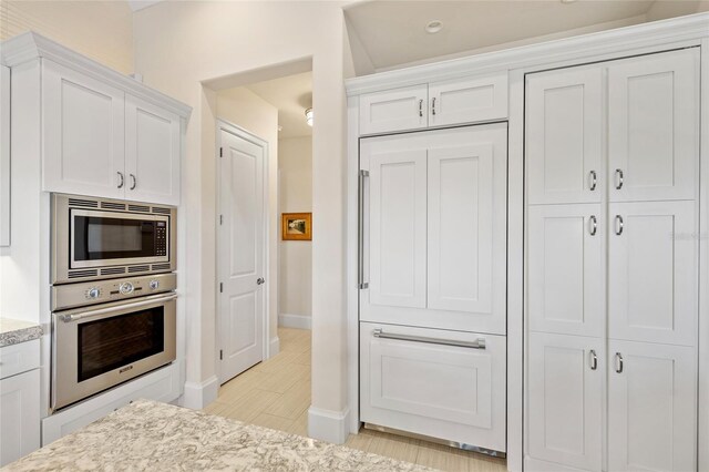 kitchen featuring stainless steel appliances, baseboards, white cabinets, light wood finished floors, and light stone countertops