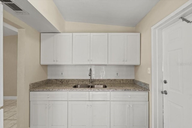 kitchen with tasteful backsplash, light stone countertops, visible vents, and a sink