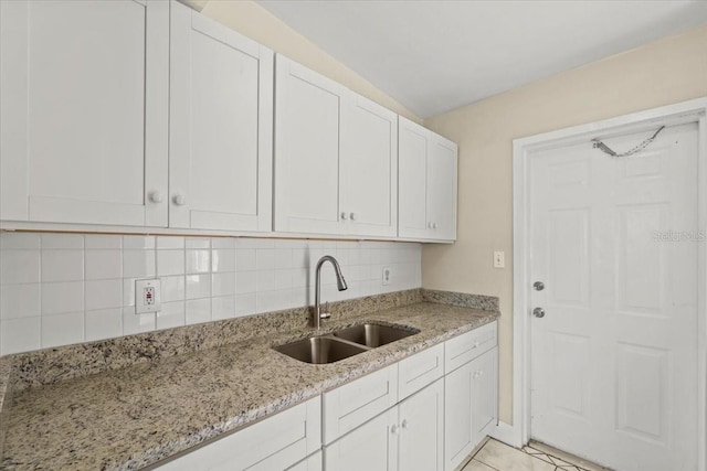 kitchen with light tile patterned floors, light stone countertops, a sink, decorative backsplash, and white cabinets