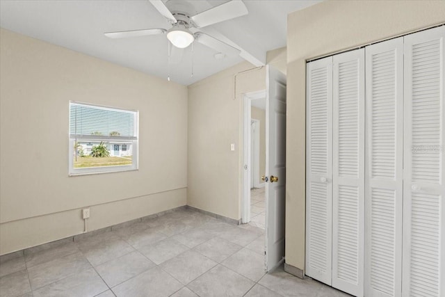 unfurnished bedroom with light tile patterned flooring, a ceiling fan, a closet, and baseboards