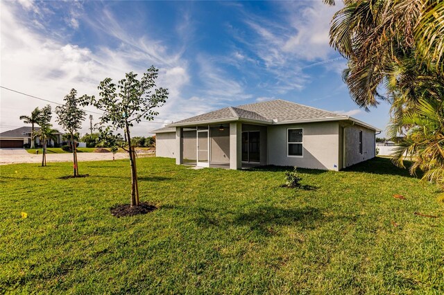 rear view of house with stucco siding, a lawn, driveway, a sunroom, and a shingled roof