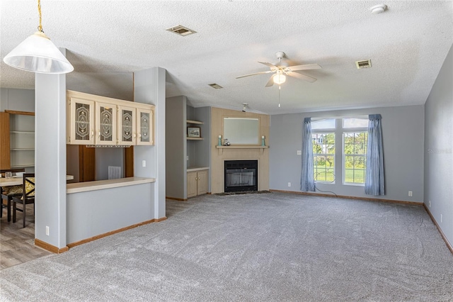 unfurnished living room with carpet flooring, a fireplace with flush hearth, a ceiling fan, and visible vents