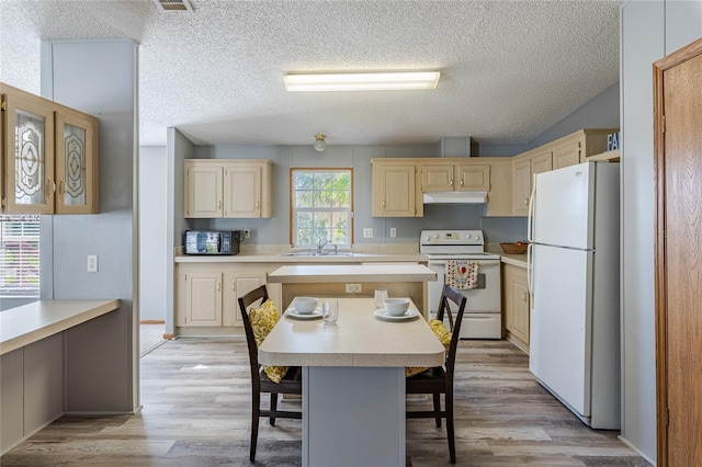 kitchen featuring a kitchen island, light countertops, light wood-style floors, white appliances, and a sink