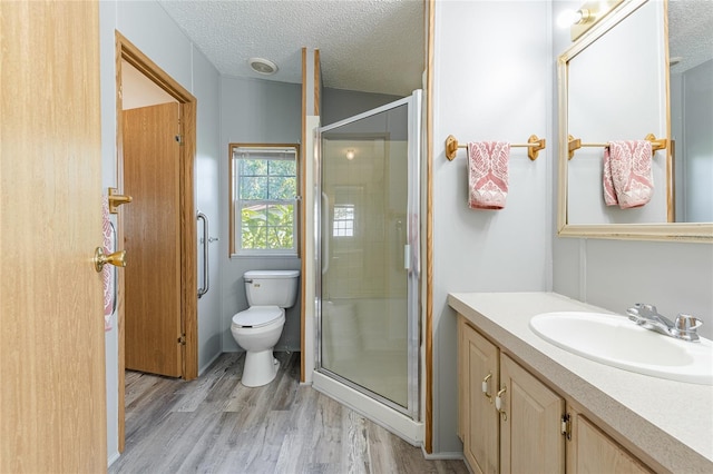 bathroom with a shower stall, toilet, vanity, wood finished floors, and a textured ceiling