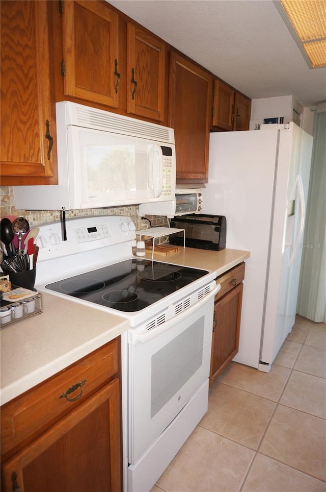 kitchen featuring white appliances, light tile patterned floors, light countertops, and brown cabinets