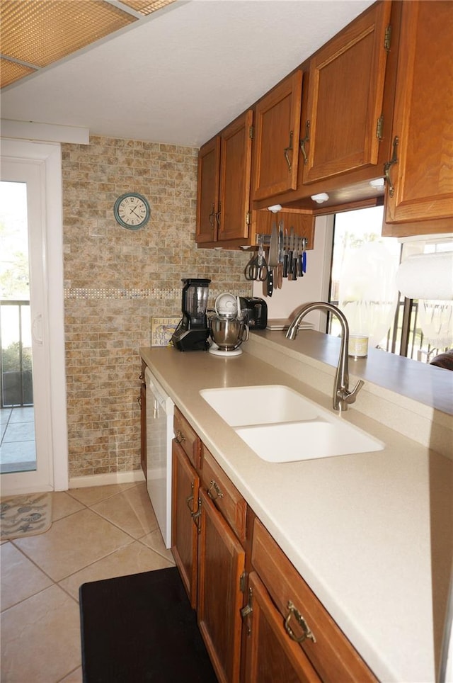 kitchen featuring brown cabinetry, light tile patterned flooring, a sink, light countertops, and dishwasher