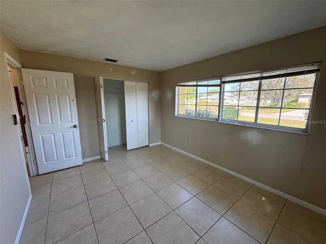 unfurnished bedroom with light tile patterned floors, visible vents, baseboards, and a closet