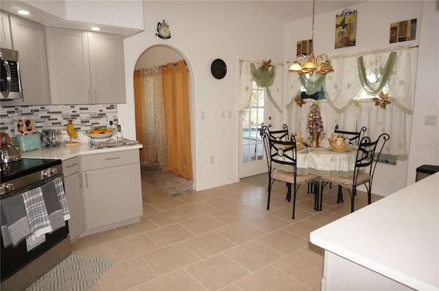 kitchen with range with electric cooktop, backsplash, arched walkways, light countertops, and light tile patterned floors