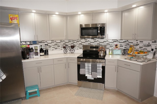 kitchen with gray cabinets, backsplash, appliances with stainless steel finishes, light tile patterned flooring, and light countertops