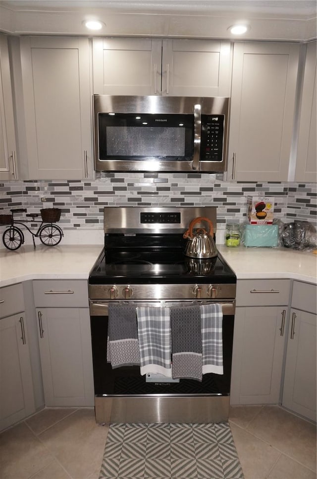 kitchen featuring gray cabinetry, appliances with stainless steel finishes, light countertops, light tile patterned floors, and decorative backsplash