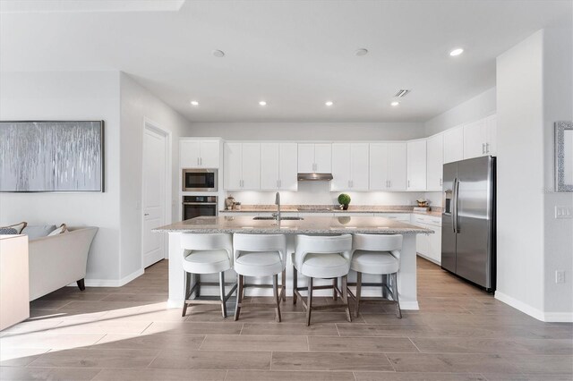 14381 Heritage Landing Blvd, Punta Gorda, FL 33955 - kitchen featuring wood tiled floor, under cabinet range hood, a center island with sink, appliances with stainless steel finishes, and a sink