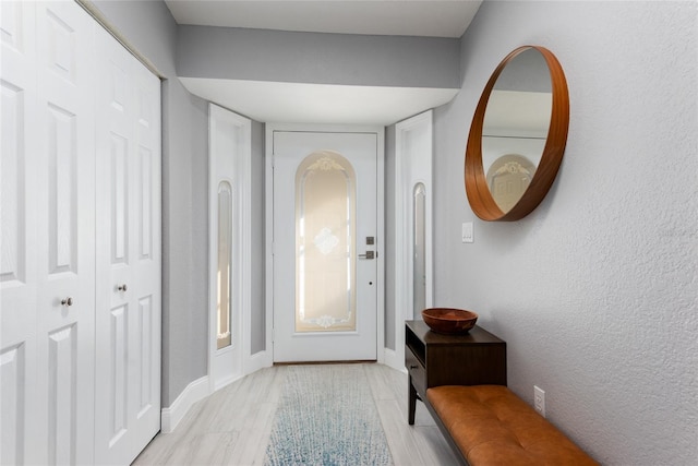 foyer entrance featuring a textured wall, light wood-type flooring, and baseboards