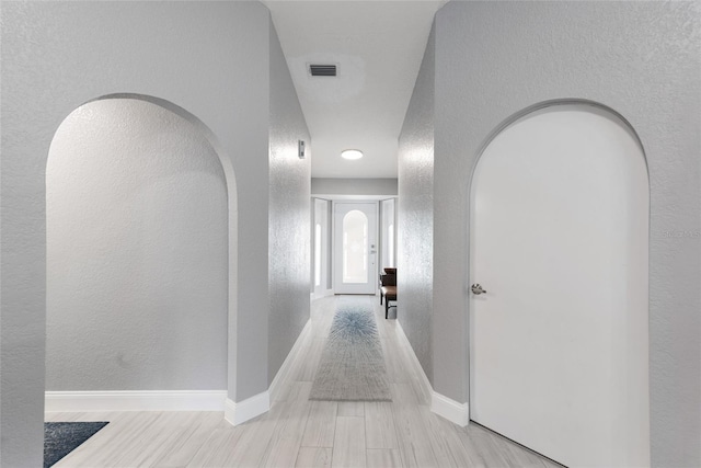 corridor featuring arched walkways, visible vents, a textured wall, and baseboards