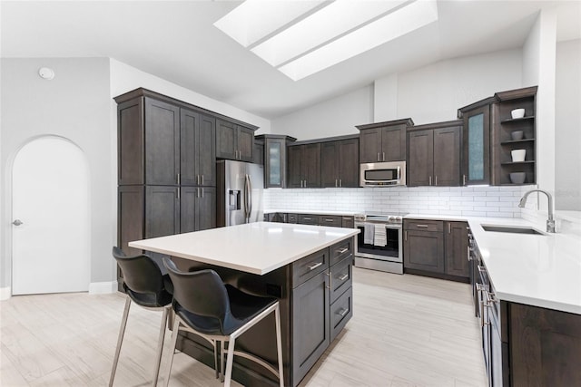 kitchen featuring open shelves, dark brown cabinetry, a kitchen bar, appliances with stainless steel finishes, and a sink