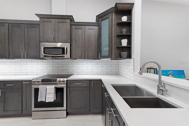 kitchen with open shelves, a sink, decorative backsplash, stainless steel appliances, and dark brown cabinets