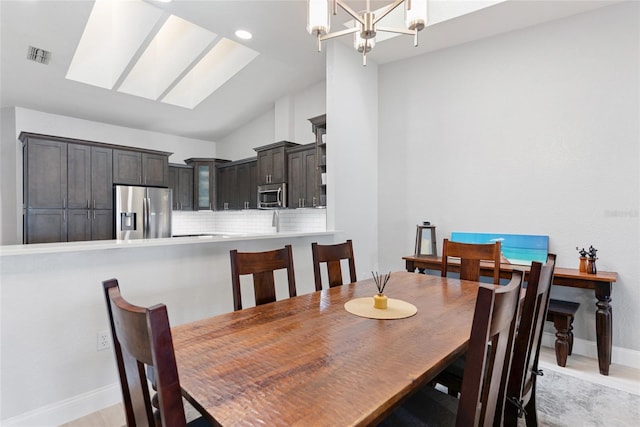 dining room with visible vents, vaulted ceiling with skylight, baseboards, and an inviting chandelier