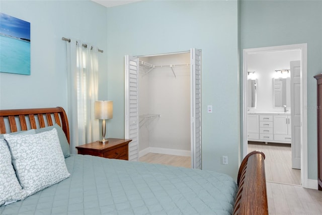 bedroom featuring wood finished floors, baseboards, a spacious closet, a closet, and ensuite bathroom