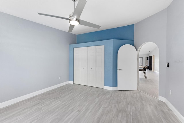 unfurnished bedroom with ceiling fan, baseboards, a closet, wood finished floors, and arched walkways