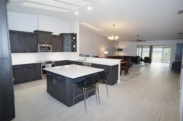 kitchen featuring a peninsula, vaulted ceiling with skylight, stainless steel appliances, light countertops, and tasteful backsplash