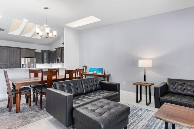 living area with visible vents, vaulted ceiling with skylight, a notable chandelier, and baseboards