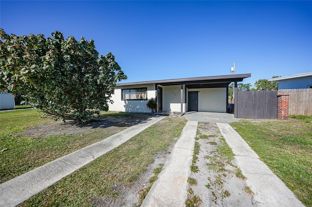 mid-century home featuring an attached carport, concrete driveway, fence, and a front yard