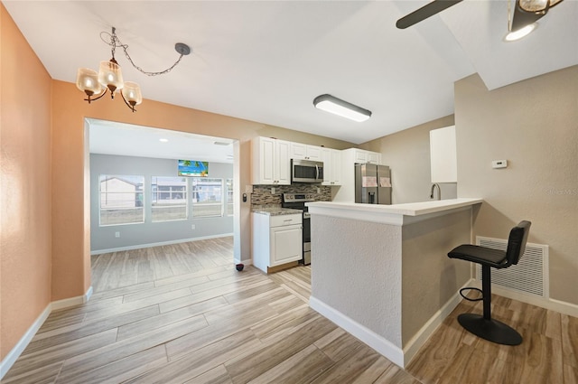 kitchen with visible vents, stainless steel appliances, decorative backsplash, white cabinets, and light wood-style floors