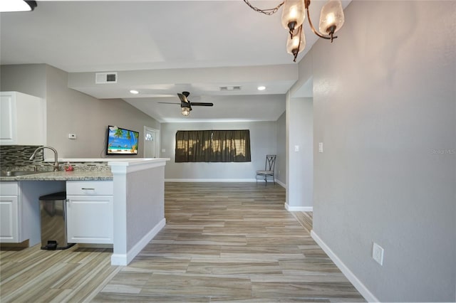 kitchen featuring visible vents, ceiling fan with notable chandelier, a sink, white cabinets, and decorative backsplash