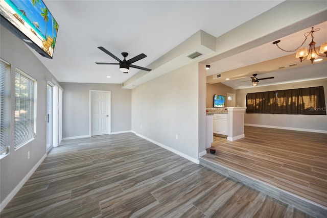 spare room featuring wood finished floors, ceiling fan with notable chandelier, visible vents, and baseboards