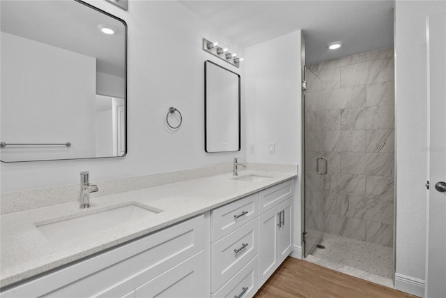 full bathroom featuring a shower stall, wood finished floors, double vanity, and a sink